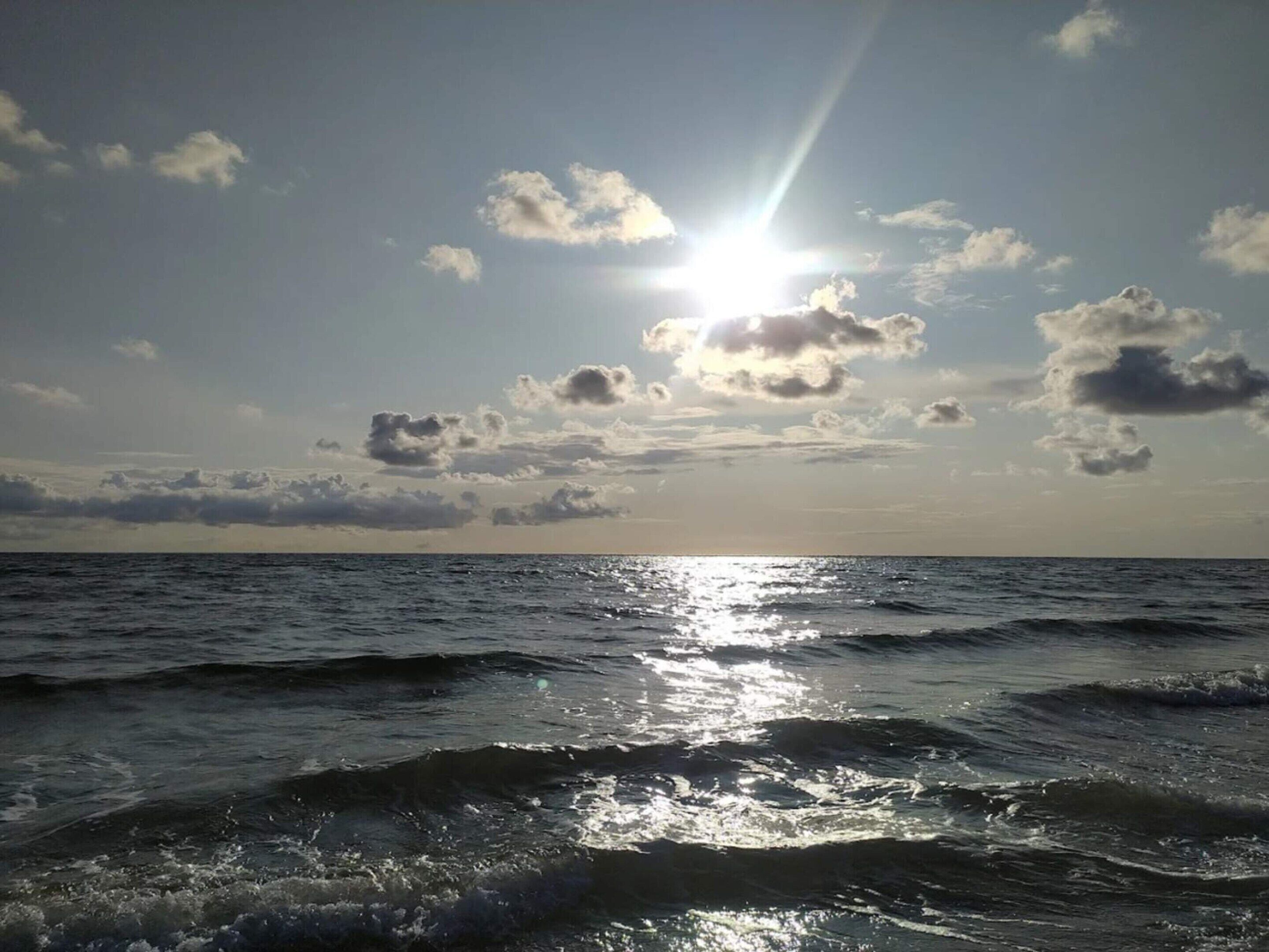 Vista de l'oceà amb la llum del sol reflectint sobre l'aigua i núvols al cel.