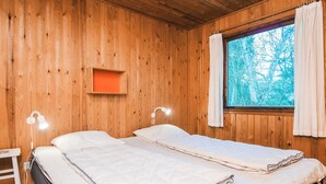 Une chambre dans un chalet en bois, avec deux lits, une table de chevet, une étagère et une fenêtre avec des rideaux.
