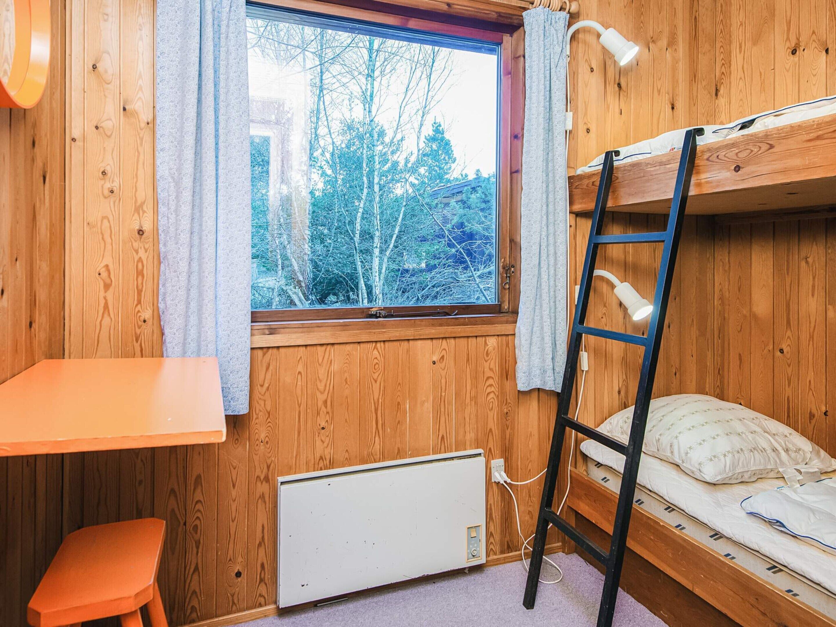 A small, wooden room with a bunk bed, a desk, and a radiator.