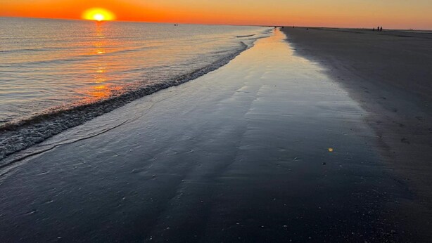 Une plage au coucher du soleil, avec des vagues calmes et un ciel dégagé.