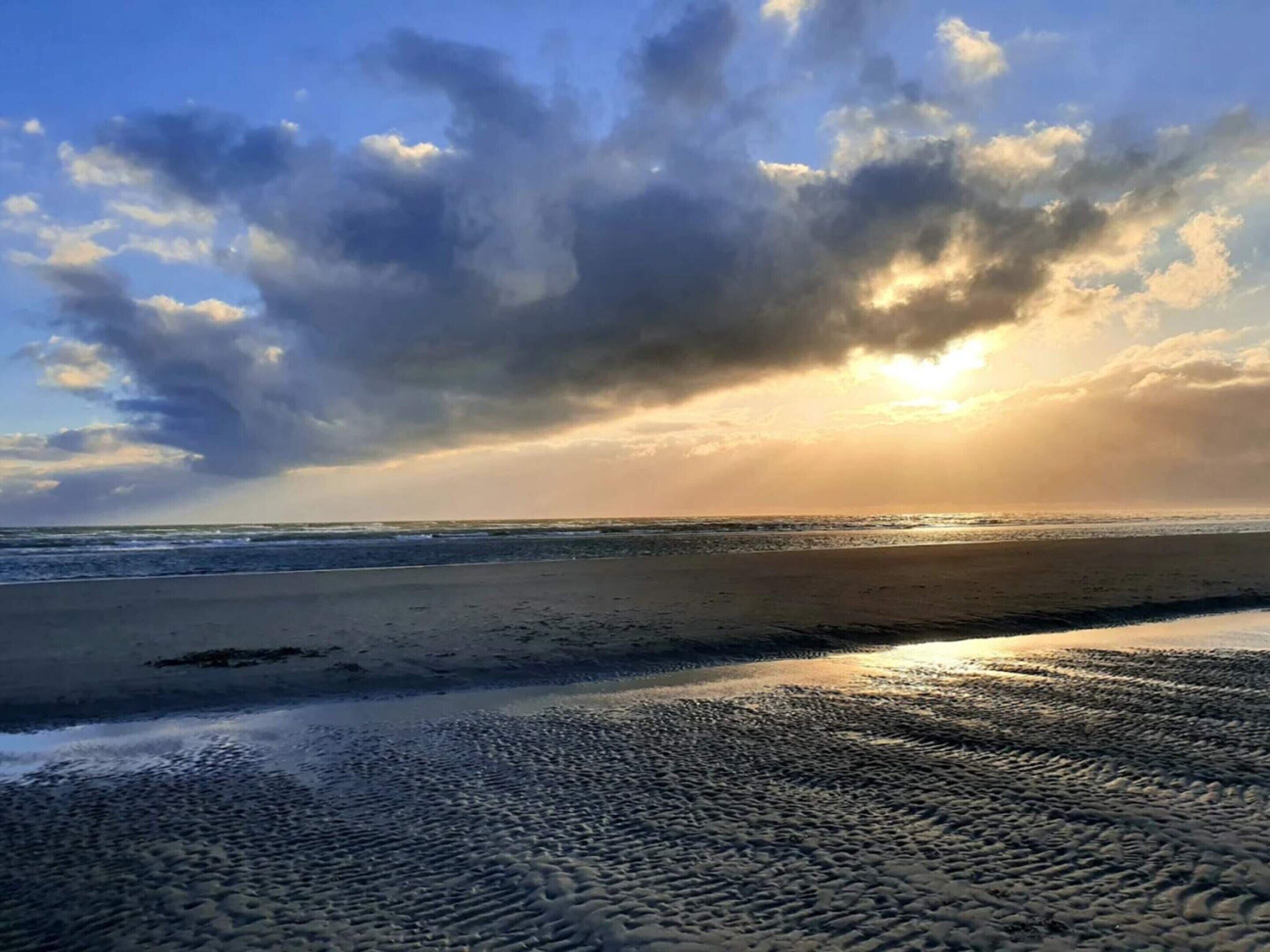 Ein Strand mit einer weiten Sandfläche und Blick auf das Meer unter einem bewölkten Himmel.