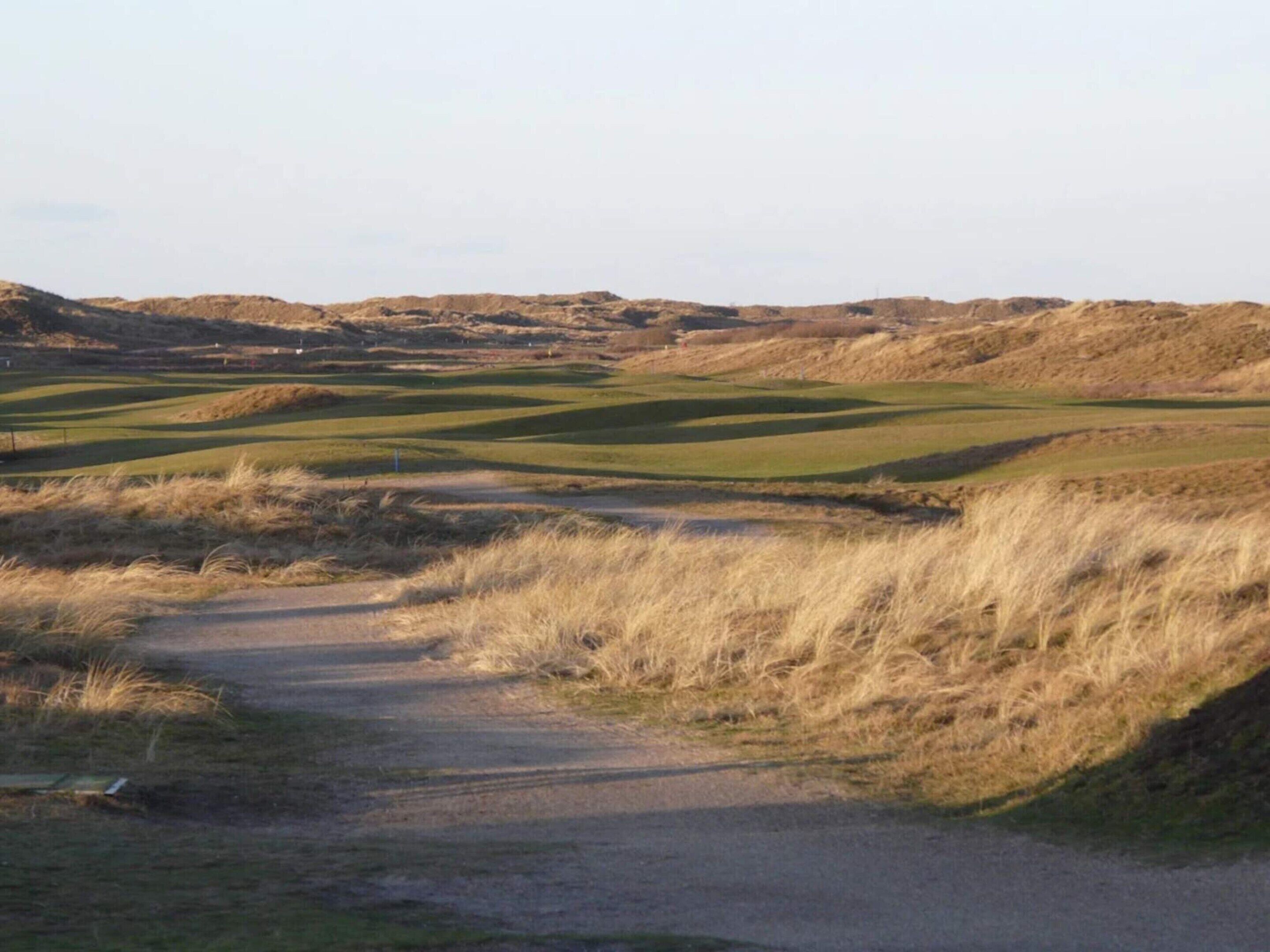 Un parcours de golf avec un sentier de terre qui traverse l’herbe.