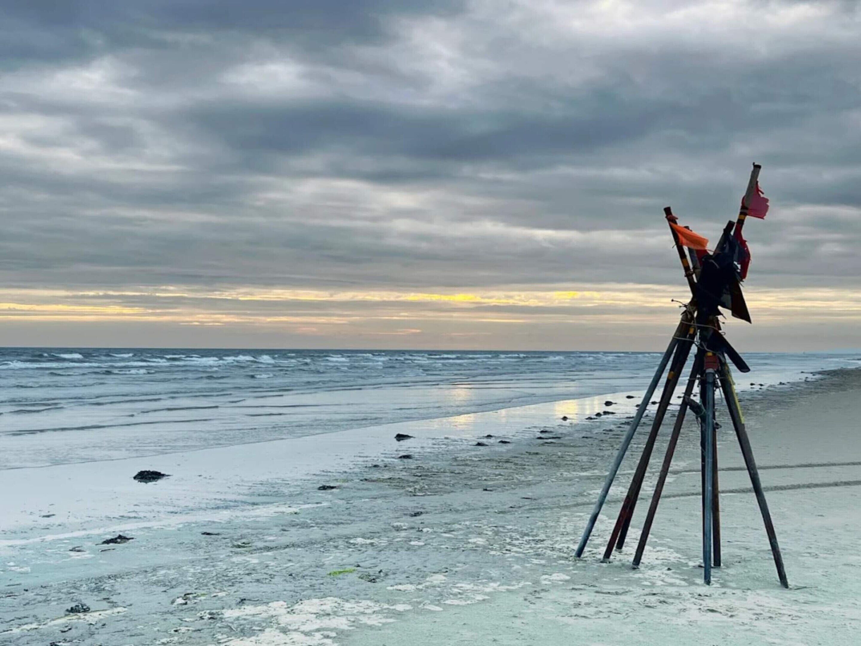 Een statief met een camera op een zandstrand, met de oceaan op de achtergrond.
