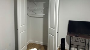 Une pièce avec une porte fermée, une armoire blanche avec des étagères, un plancher en bois et un téléviseur posé sur un meuble.