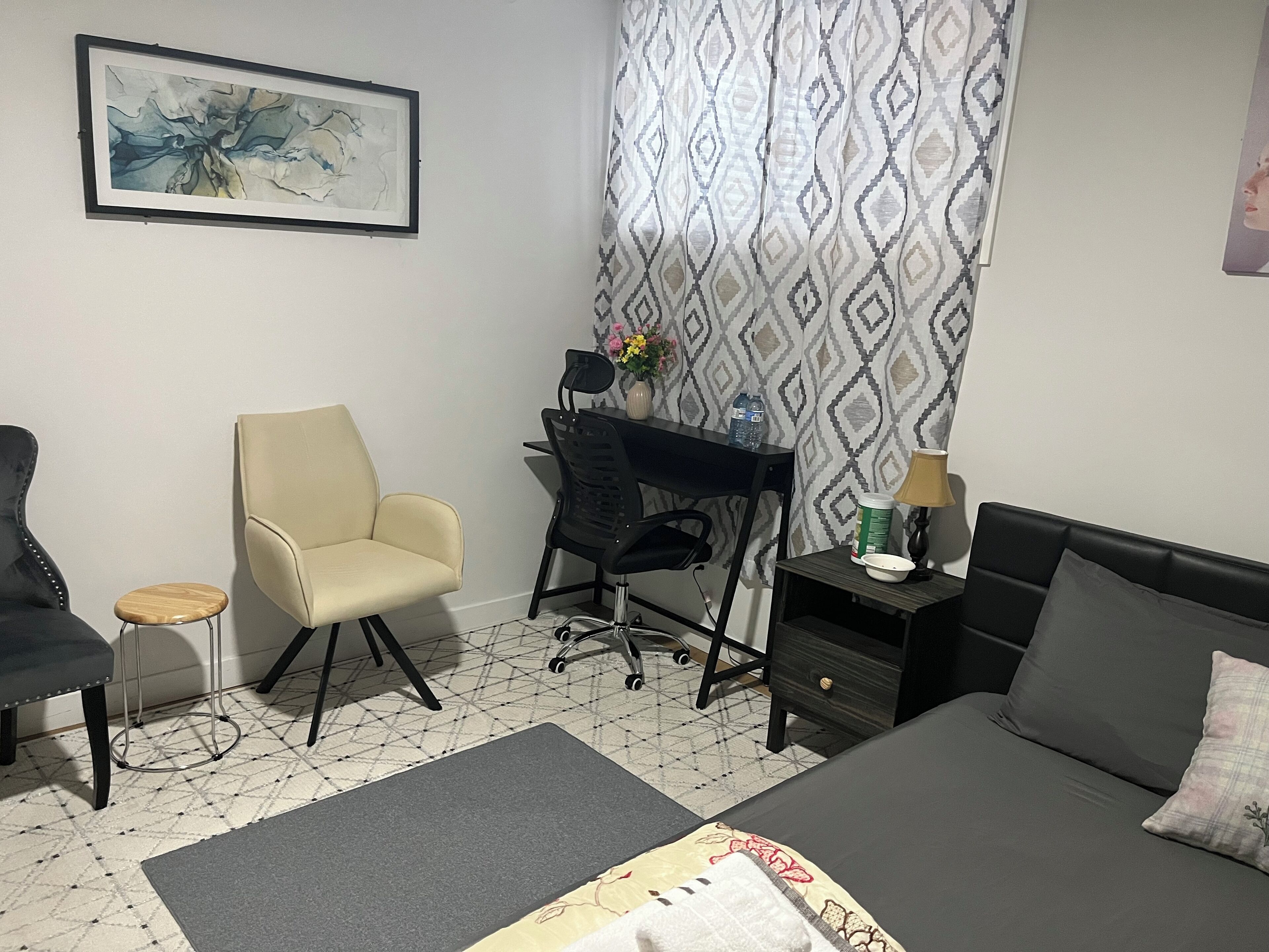 Een moderne slaapkamer met een bed, een bureau, een stoel en een klein krukje.