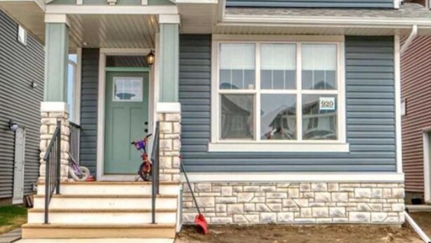 Une maison à deux étages avec un porche à l’avant, des fondations en pierre et le numéro « 920 » inscrit sur la fenêtre.