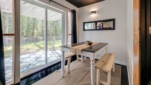 Een eethoek met een tafel en banken, grote ramen en uitzicht op een tuin.