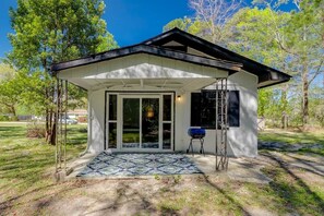 Een modern huis met een overdekte veranda, grote glazen deuren en een barbecue in de tuin.