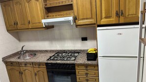 Una cocina con armarios de madera, un lavamanos de acero inoxidable, una estufa a gas, un horno empotrado y un refrigerador blanco.