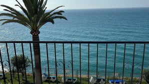 Un balcon avec vue sur la mer, un palmier et un panier de fruits sur la table.
