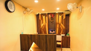 A reception area with a wooden reception desk, a wall-mounted clock, and two wall fans. - DhamStay Hotel Santosh Inn Near Temple (Puri)