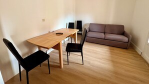 A room with a wooden table, two black chairs, a brown sofa, and a ceiling fan.