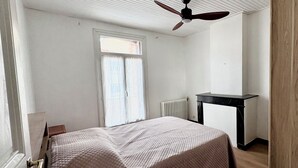 A bedroom with a bed, a ceiling fan, a window, and a radiator.