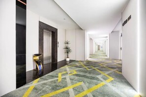 Pasillo de hotel con alfombra estampada, una mesa de recepción y una planta en maceta.