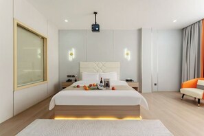 Quarto de hotel moderno com uma cama grande, mesas de cabeceira, um projetor e vista para a cidade.
