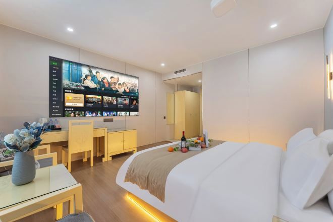 Quarto de hotel com cama, escrivaninha, cadeira, televisão fixada na parede e espelho.