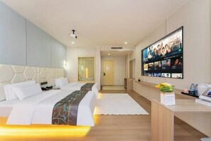 Quarto de hotel com uma cama grande, uma mesa de trabalho com um computador e uma televisão exibindo várias telas.