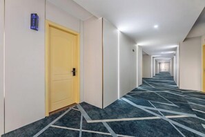 Un pasillo de hotel con alfombra estampada, una puerta amarilla y un accesorio de iluminación en el techo.