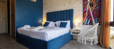 Un dormitorio con una cama grande, aire acondicionado de pared, un cuadro abstracto y colorido, y una silla colgante.