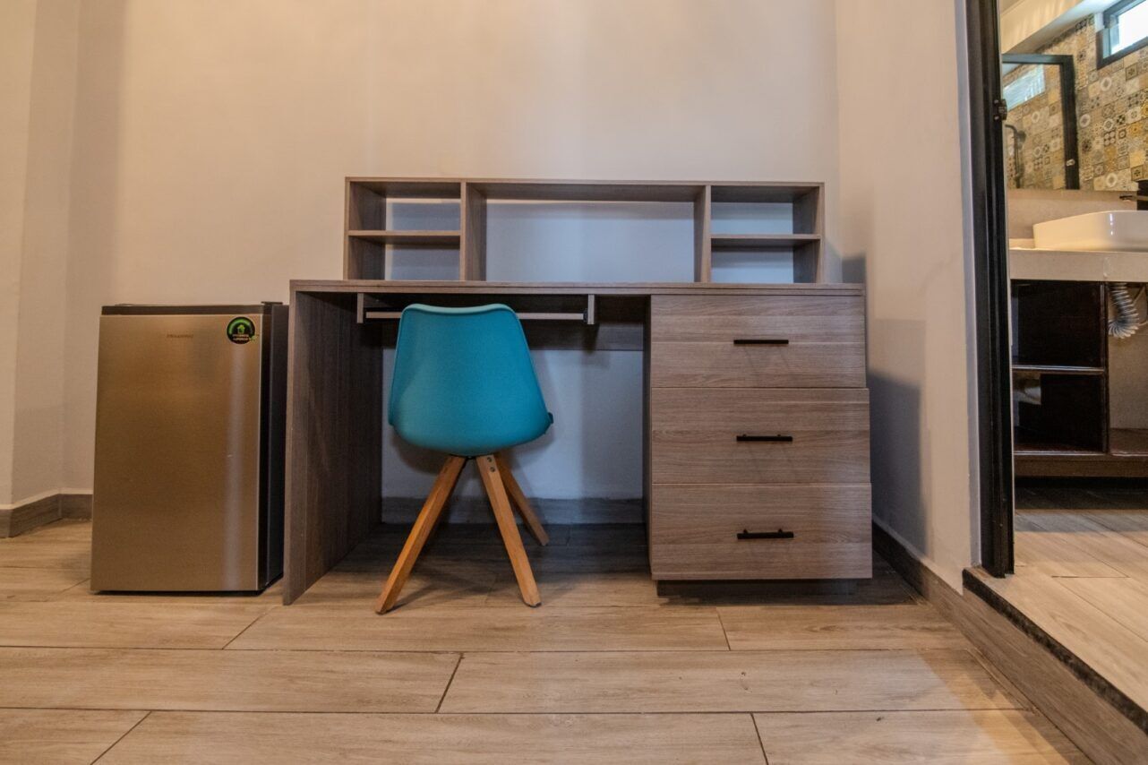Eine kleine Küchenzeile mit integriertem Kühlschrank, einem Holztisch mit Schubladen und einem stuhlfarbenen Stuhl.