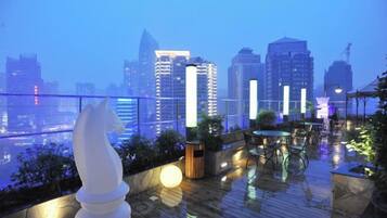 A rooftop terrace with a city skyline view, seating areas, and a decorative horse sculpture.