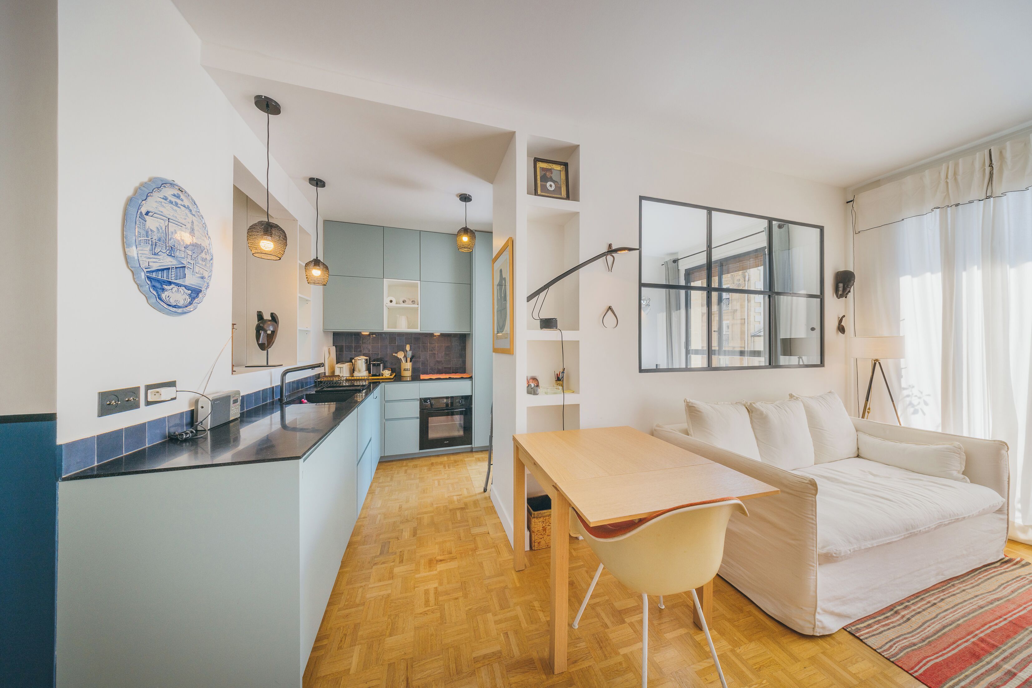 Una cucina moderna con mobili azzurri, un tavolo da pranzo in legno e un divano bianco nella zona soggiorno.