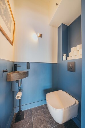 Une salle de bain moderne dotée d’un lavabo intégré, de toilettes et d’un porte-rouleau de papier toilette fixé au mur.