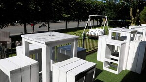 Outdoor seating areas with white tables and benches, surrounded by trees and a swing set. - 5 Star Holiday Home in Wangerland (Wangerland)