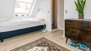 Un dormitorio con cama, escritorio, planta en maceta y alfombra estampada.