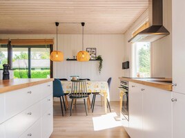 Una cocina moderna con armarios de madera, una mesa de comedor con sillas, lámparas colgantes y vistas al exterior.