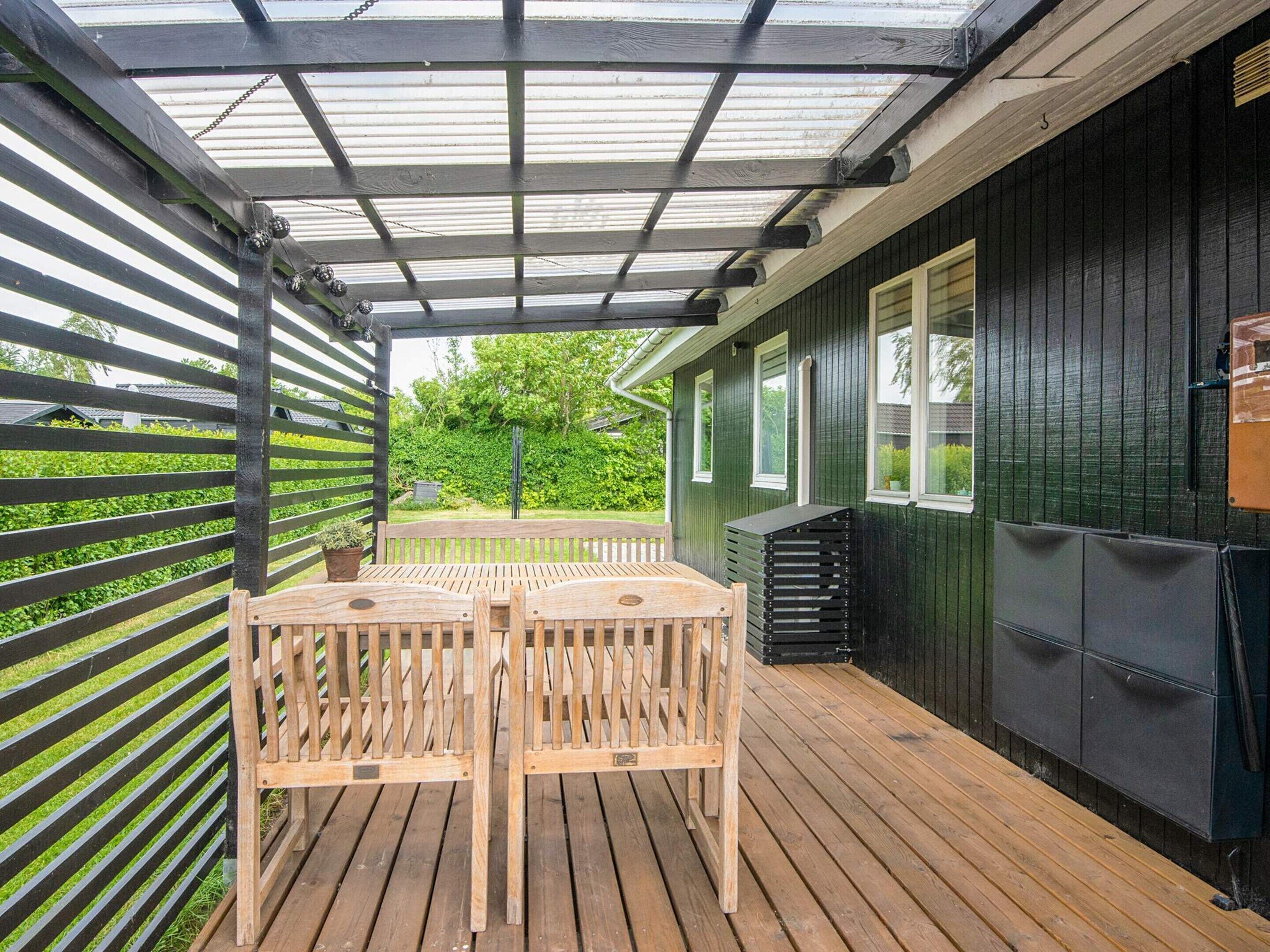 Puinen terassi, jossa on pergola, pöytä ja tuolit sekä musta kaappi.