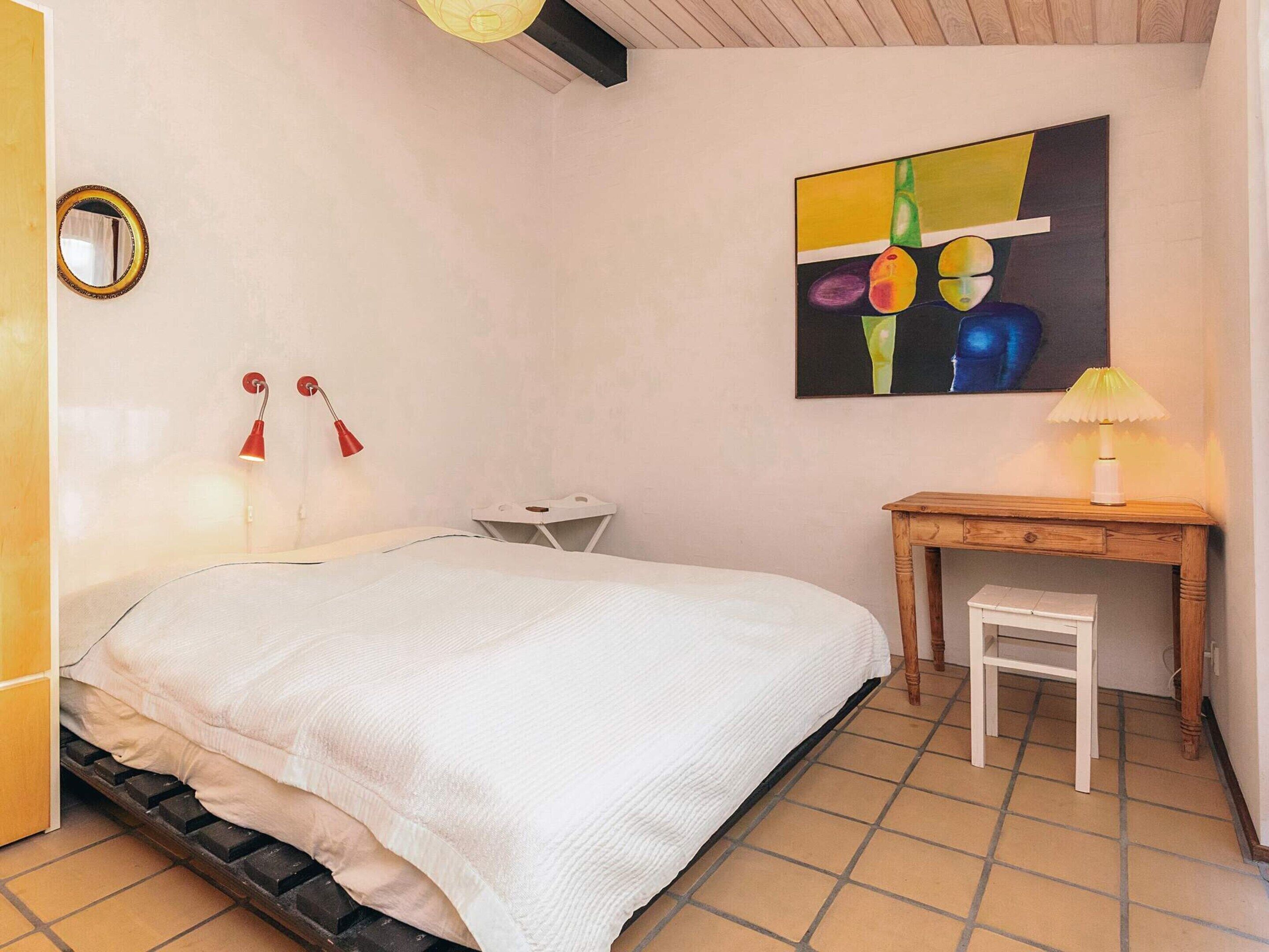 A bedroom with a bed, a desk, a chair, a lamp, and a painting on the wall.