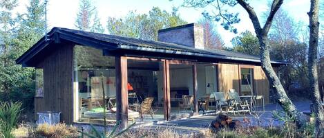 A modern house with large glass windows, a wooden exterior, and a patio area with outdoor furniture.