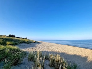 A beach with sand and grass, a clear sky, and a calm sea.