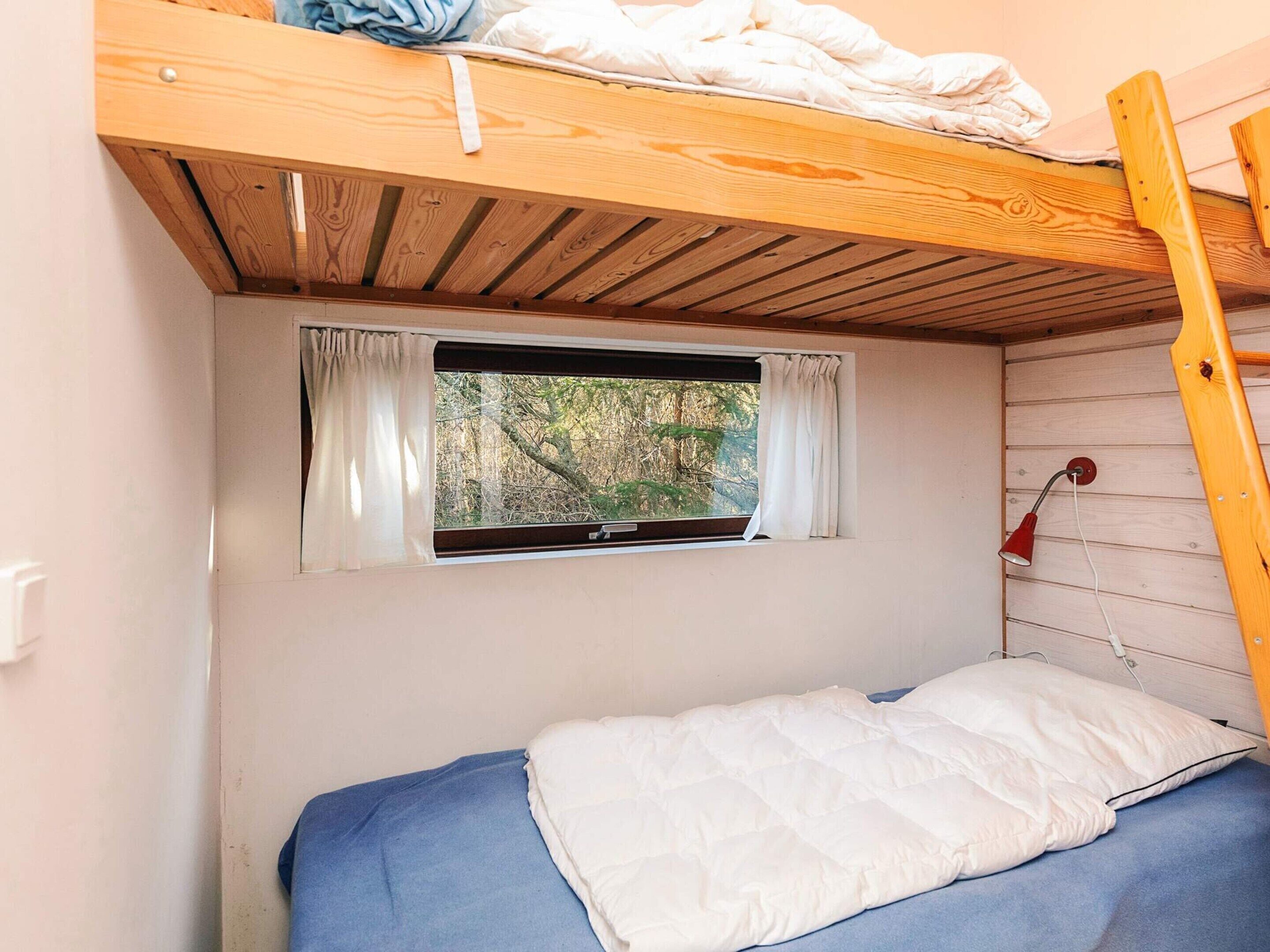 Een kleine eenpersoonskamer met een stapelbed er boven, een raam met gordijnen en een rode lamp aan de muur.