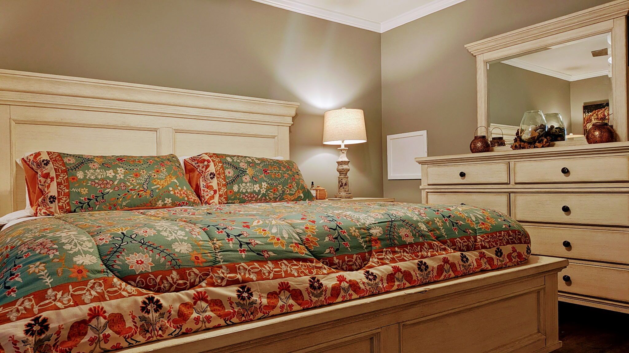 A bedroom with a bed, a nightstand, a dresser, and a mirror.