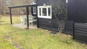 A black wooden house with a covered patio, a window, and a small tree. - 5 Person Holiday Home in Vaeggerlose (Vaeggerlose)