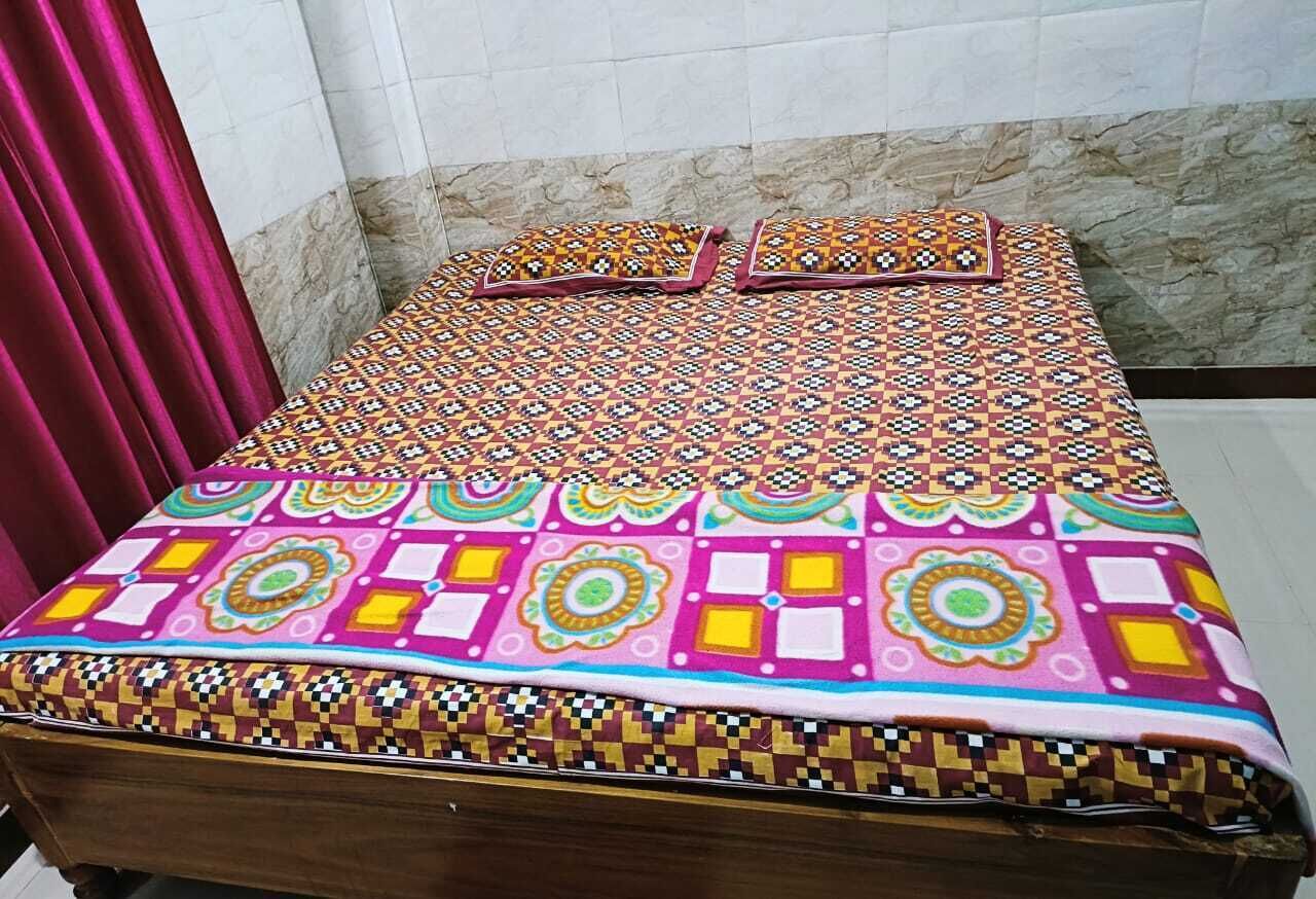 Una cama con una colcha y almohadas de estampado colorido, un cabecero de madera y una pared de mármol al fondo.