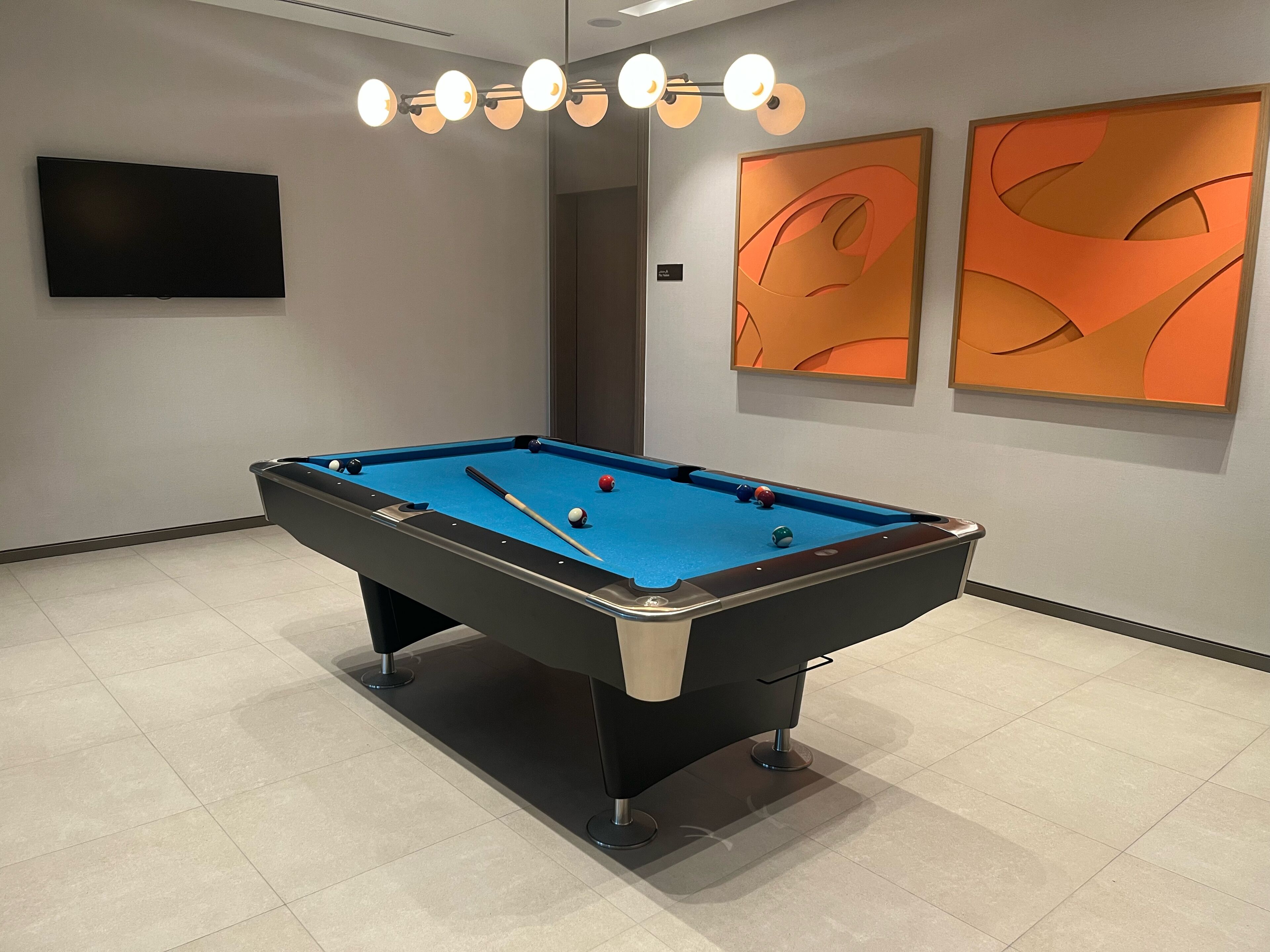 A pool table with balls, a television, and abstract wall art.
