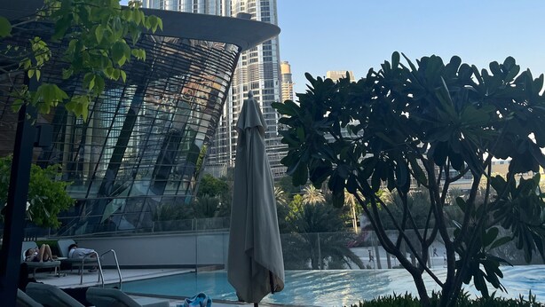 A high-rise building with a modern design, a pool area with lounge chairs, and a clear blue sky.