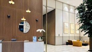 A modern reception area with a marble reception desk, wooden paneling, and a large potted plant.