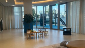 A spacious lobby with a large potted plant, wooden furniture, and a view of a playground through large glass doors.