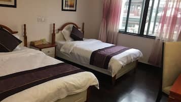 A hotel room with two beds, a nightstand, a chair, and a window with curtains.