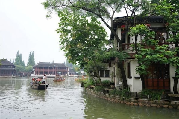 A traditional building with a waterway in front, boats, and greenery.