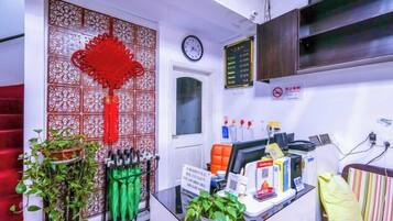 A reception area with a desk, a clock, a wall-mounted menu board, and a decorative red hanging ornament.