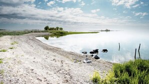 A tranquil lakeside scene with a sandy beach, calm water, and a clear sky. - 5 Star Holiday Home in Lottorp (Löttorp)