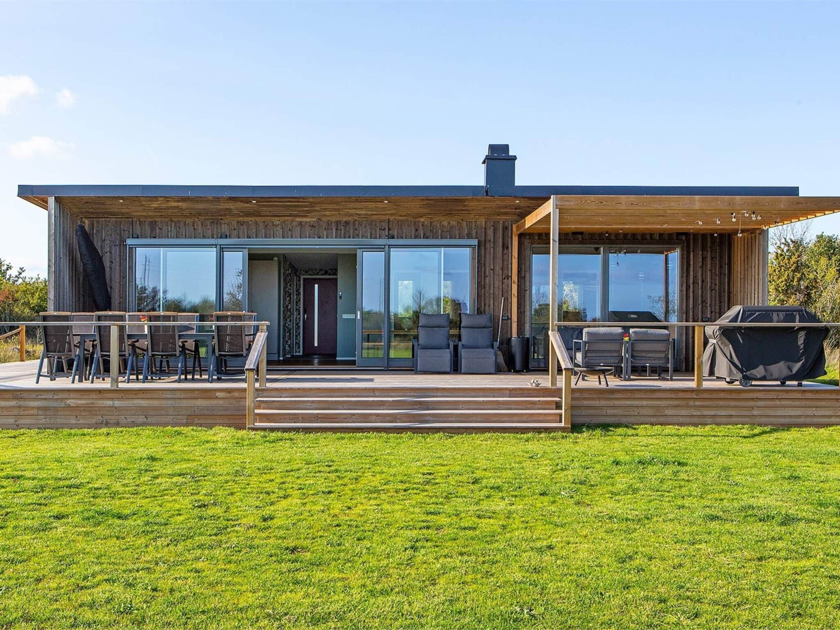 A modern house with a wooden deck, large glass doors, outdoor seating, and a barbecue area.