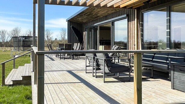 A wooden deck with outdoor seating, large windows, and a pergola with string lights. - 5 Star Holiday Home in Lottorp (Löttorp)