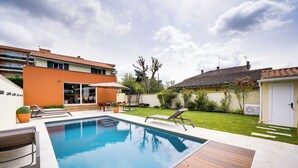 A modern outdoor swimming pool with wooden decking, a sun lounger, and a small patio area.