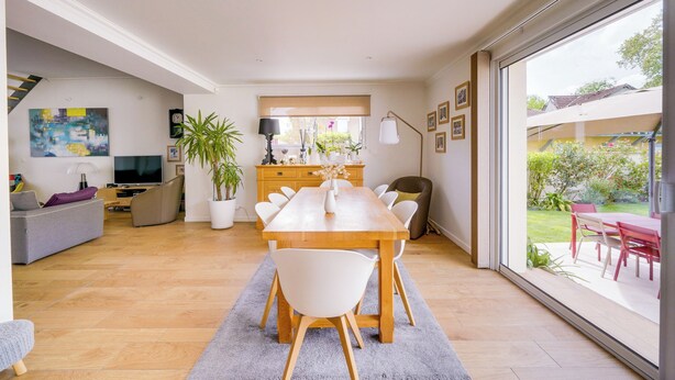 A modern living room with a dining area, a TV, a sofa, and a large window.